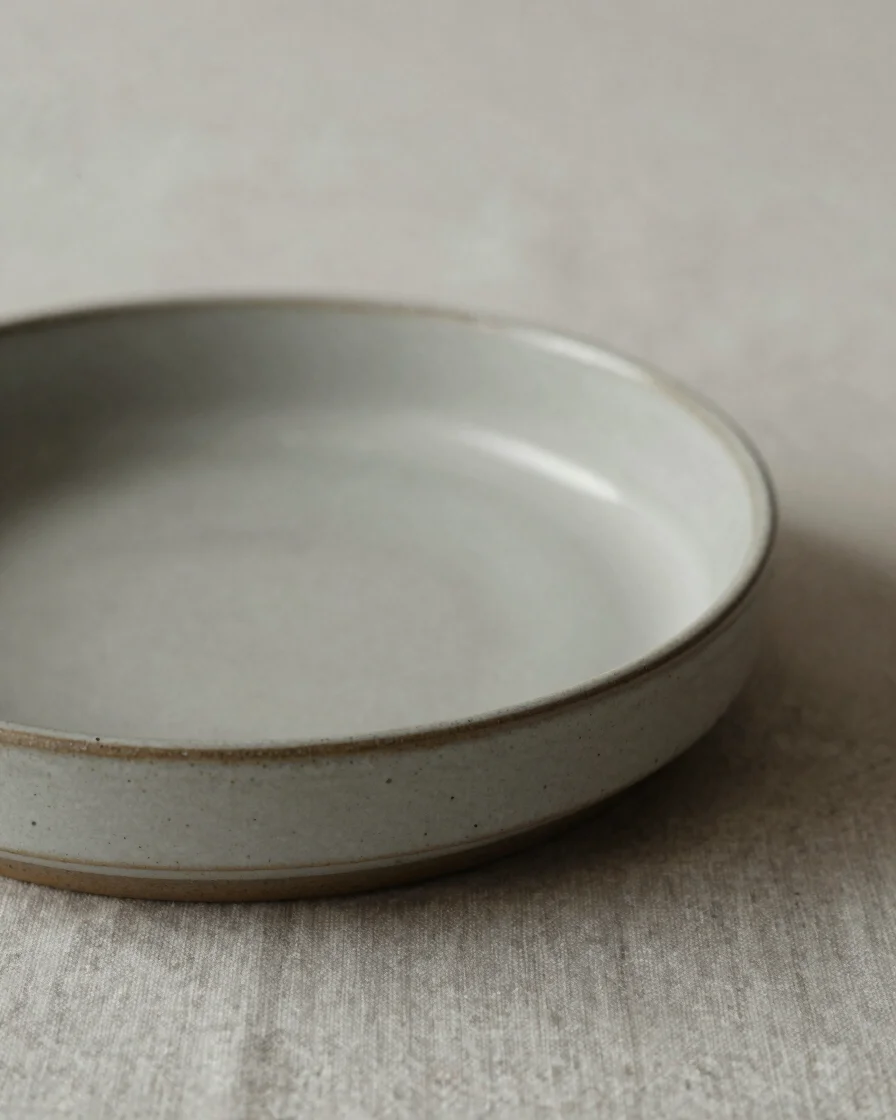 Close, soft-daylight detail of a ceramic or metal object resting on a neutral linen surface, showing surface finish and